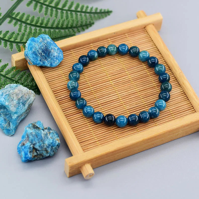 Bracciale in perle di apatite blu su un supporto di legno con pietre blu a sinistra